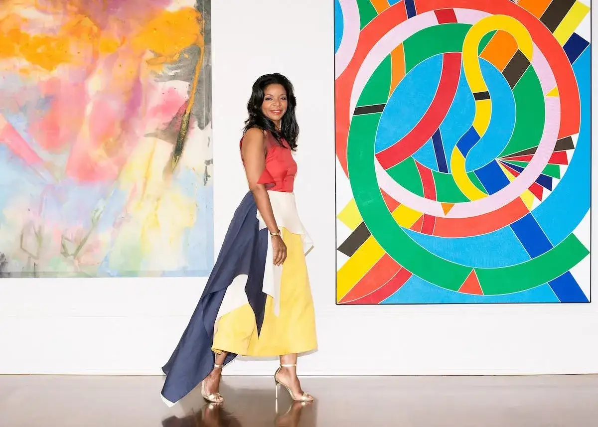 Pamela Joyner poses in a vibrant gallery, her colorful skirt mirroring the abstract art surrounding her.