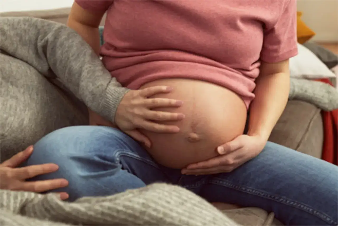 Gravid mage med händer som smeker, kanske tecken på stressad bebis i magen.