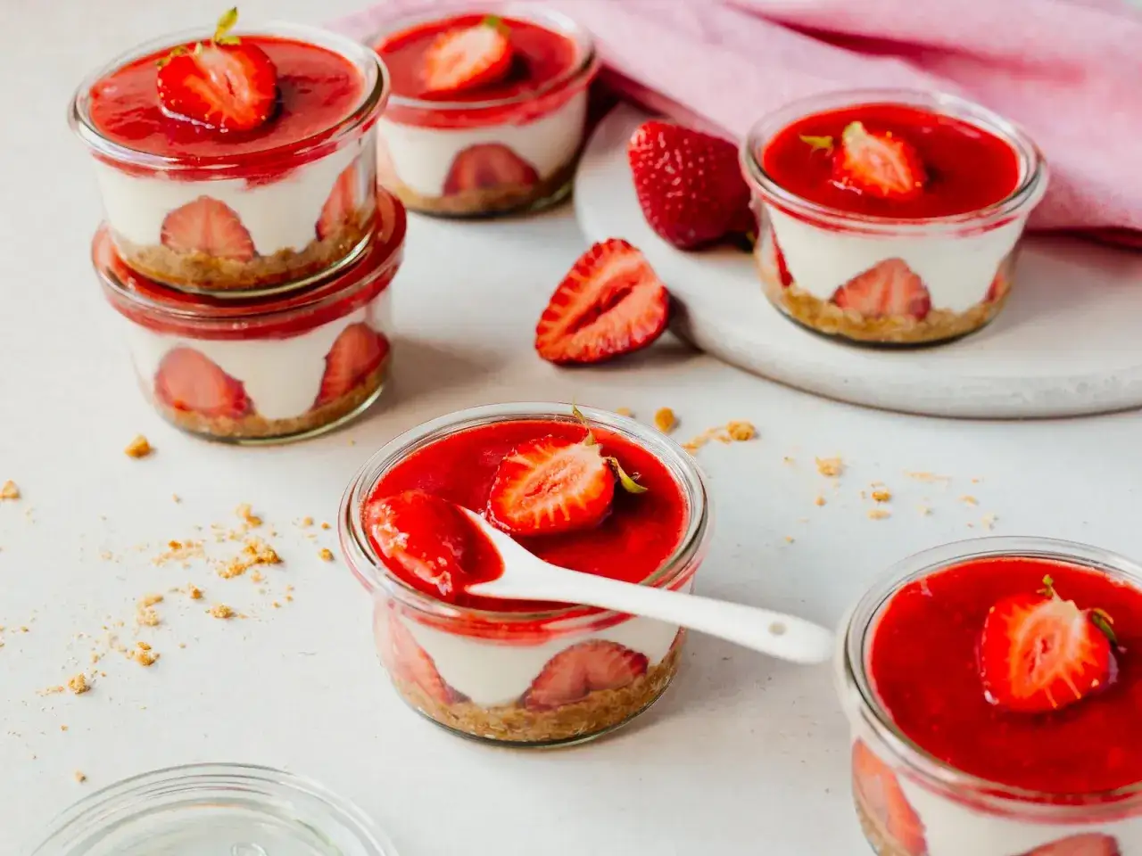 Mehrere Erdbeer-Desserts im Glas mit Frischkäsecreme, Erdbeeren und rotem Fruchtpüree, garniert mit Erdbeerscheiben.