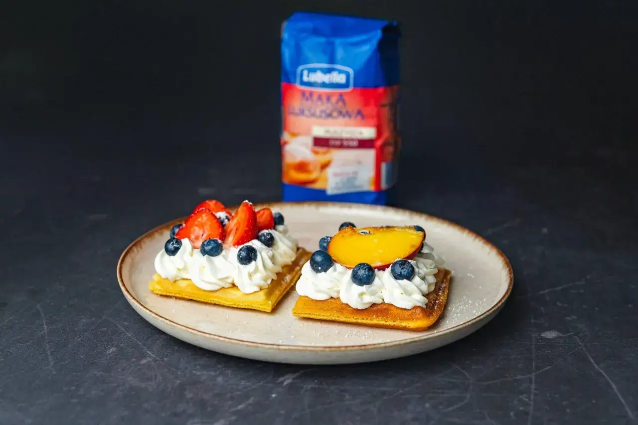 Pyszne gofry z bitą śmietaną, truskawkami, bor&oacute;wkami i brzoskwinią. Idealny przepis na deser, do kt&oacute;rego przyda się mąka z niebieskiej paczki.