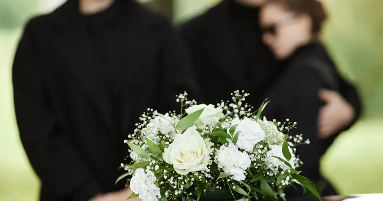 Białe kwiaty na pogrzebie. Ludzie w żałobie, pytanie ile trwa żałoba, jest indywidualne.