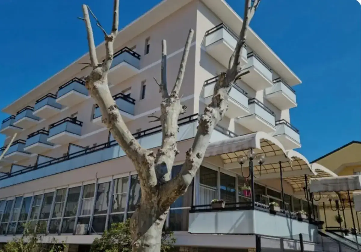 Edificio moderno con balconi e vetrate, un grande albero spoglio in primo piano. Il **Kursaal Bellaria** attende i suoi ospiti sotto un cielo azzurro.