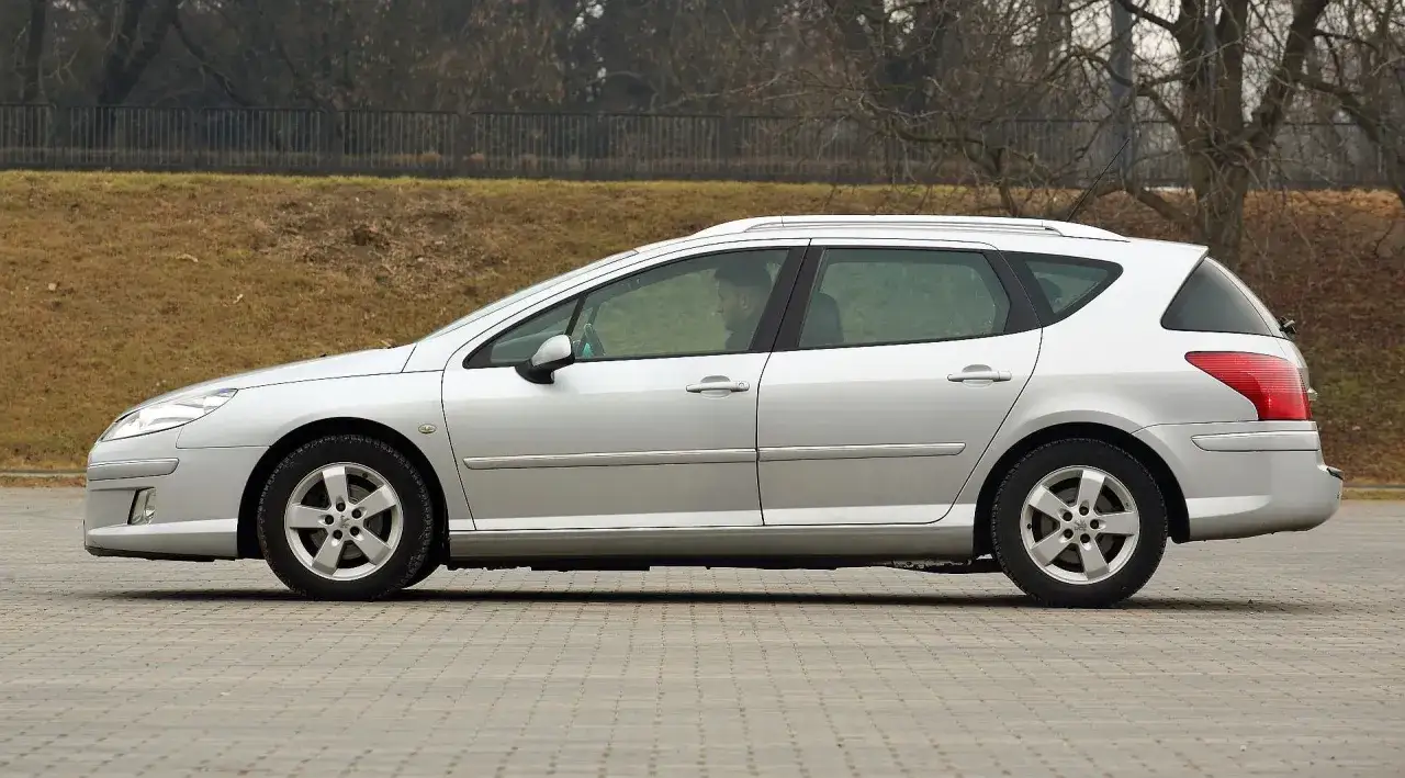 Srebrne kombi Peugeot 407, widziane z boku. Kierowca siedzi za kierownicą. Wiele osób szuka peugeot 407 opinie przed zakupem.