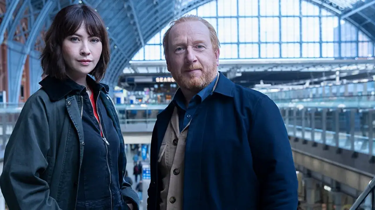 Tv&aring; detektiver, en kvinna och en man, st&aring;r i en stor, modern byggnad. De ser ut att vara p&aring; ett uppdrag som Chelsea detective.
