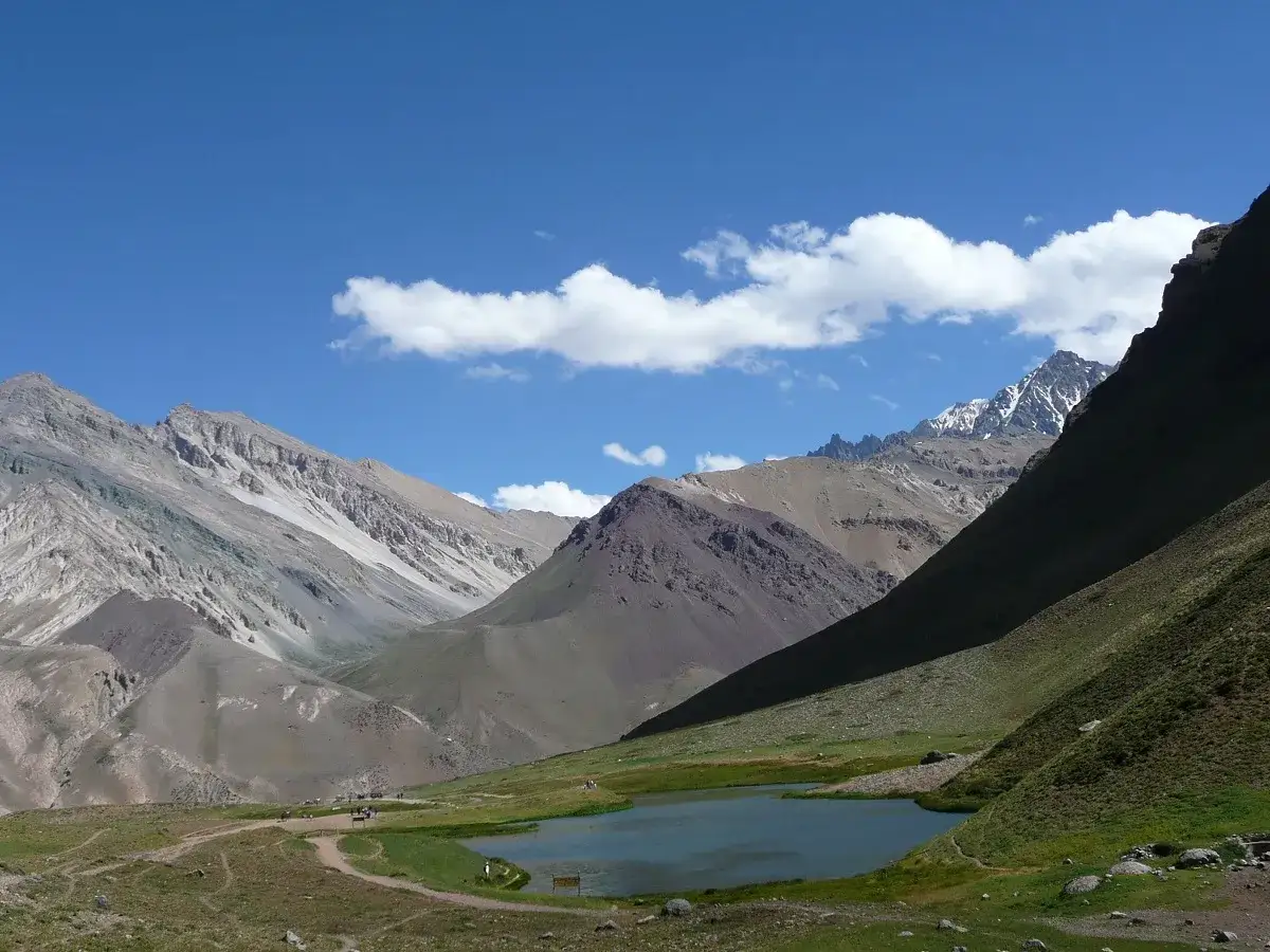 Majestatyczne góry z Aconcagua w oddali, z jeziorem i zielonymi zboczami w dole.