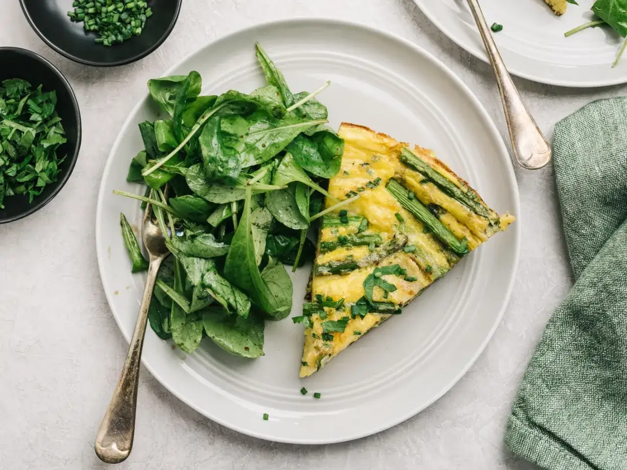 Una fetta di frittata di asparagi selvatici, soffice e dorata, servita con un'insalata fresca.