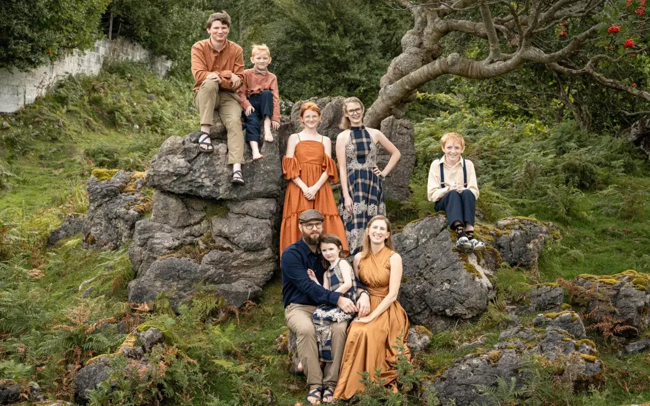 Famiglia felice in Scozia con bambini, seduti su rocce tra felci e alberi.