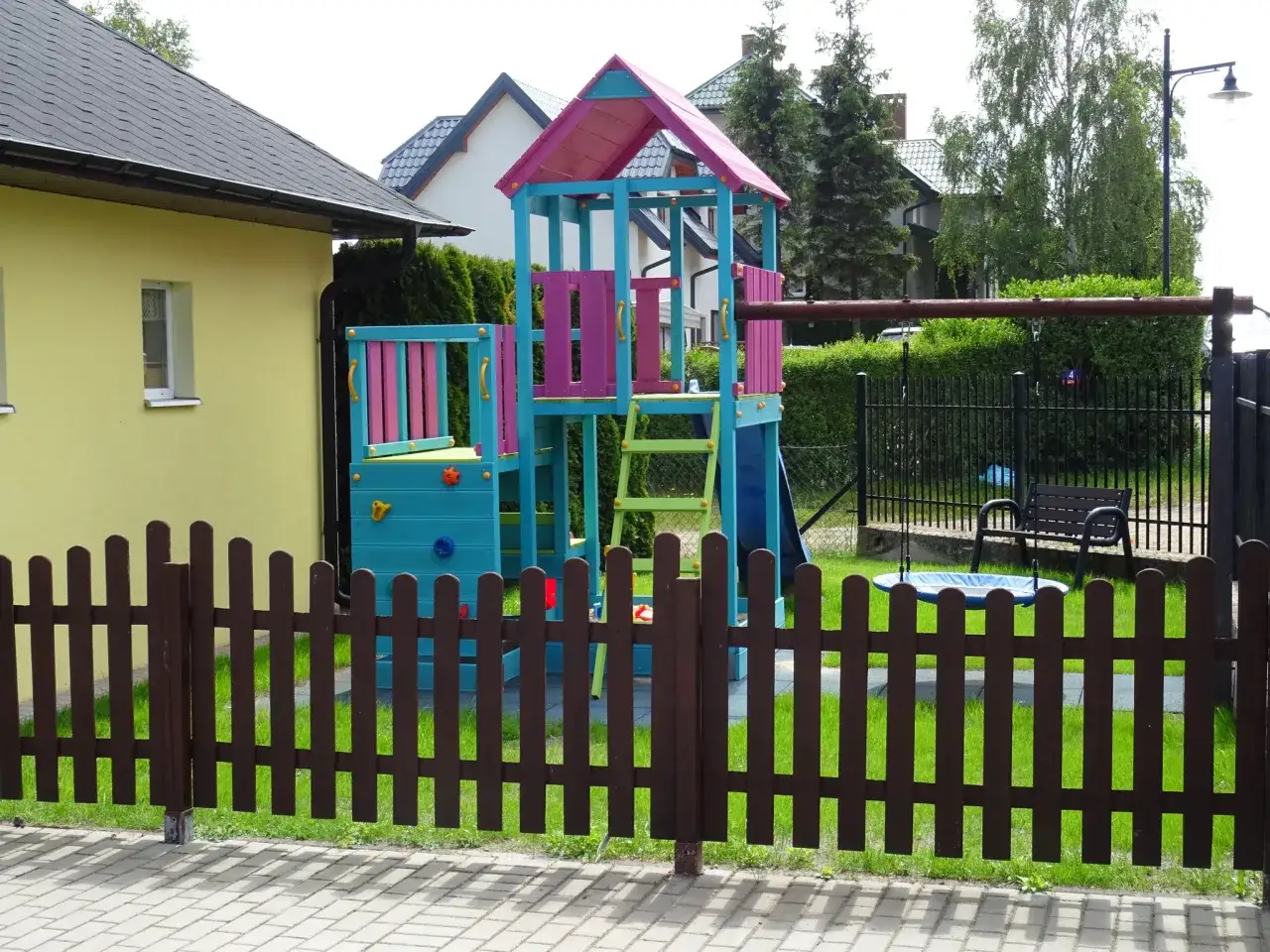 Kolorowy plac zabaw przy willi Global w Jastrzębiej Górze. Zjeżdżalnia, drabinka i huśtawka czekają na dzieci.