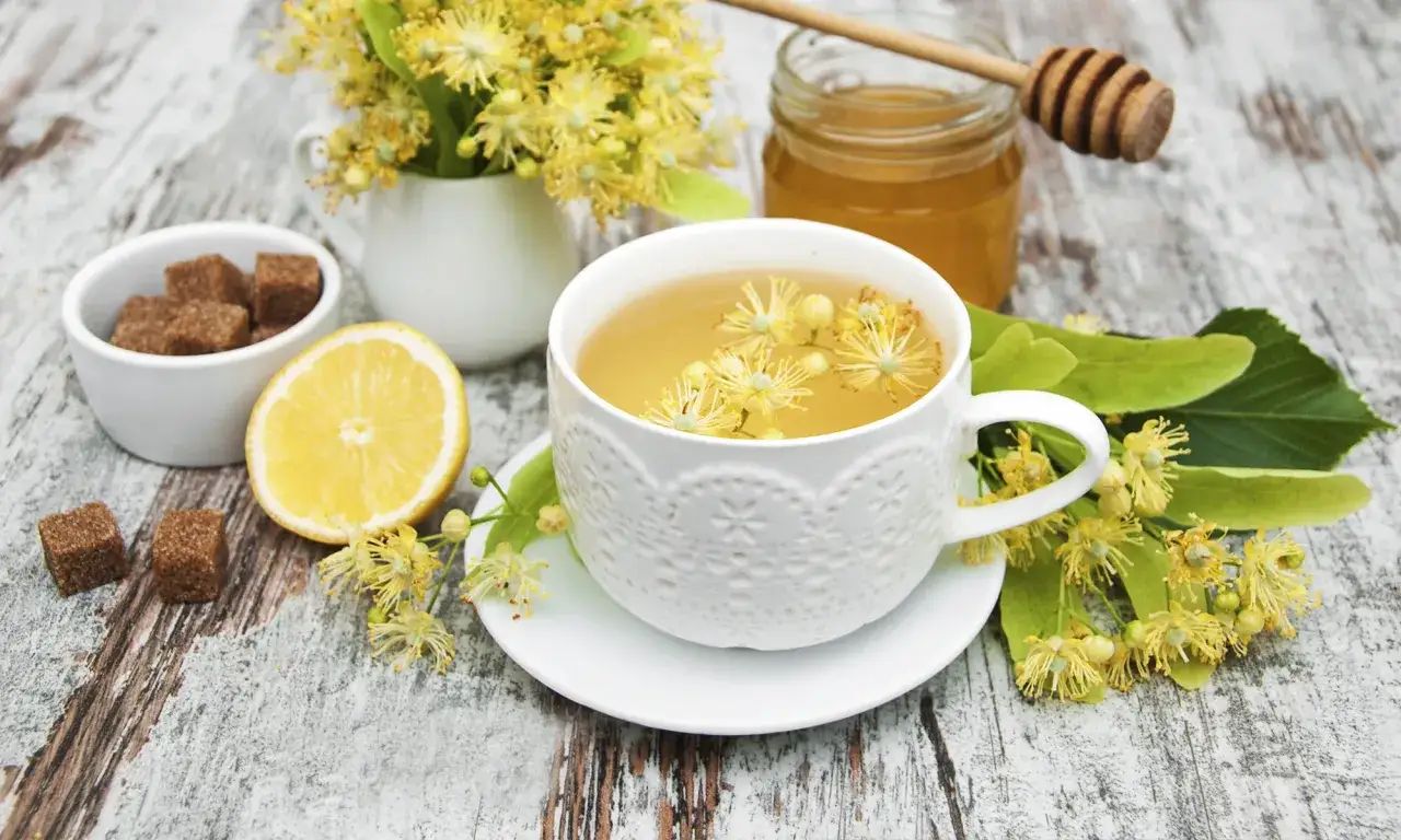 Aromatyczna herbata z lipy na przeziębienie, z miodem, cytryną i cukrem trzcinowym, otoczona świeżymi kwiatami lipy.