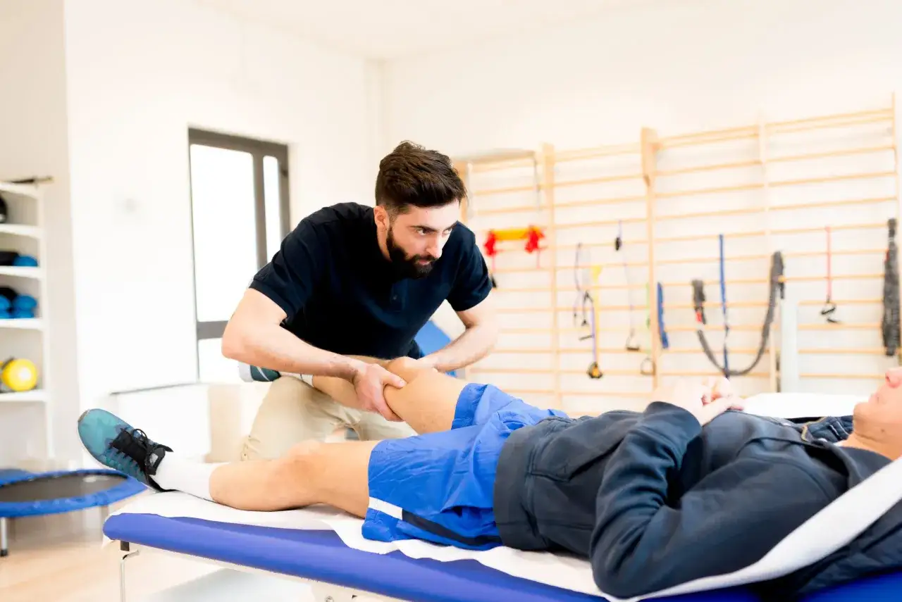 Fizjoterapeuta wykonuje masaż sportowy na nodze pacjenta leżącego na kozetce.