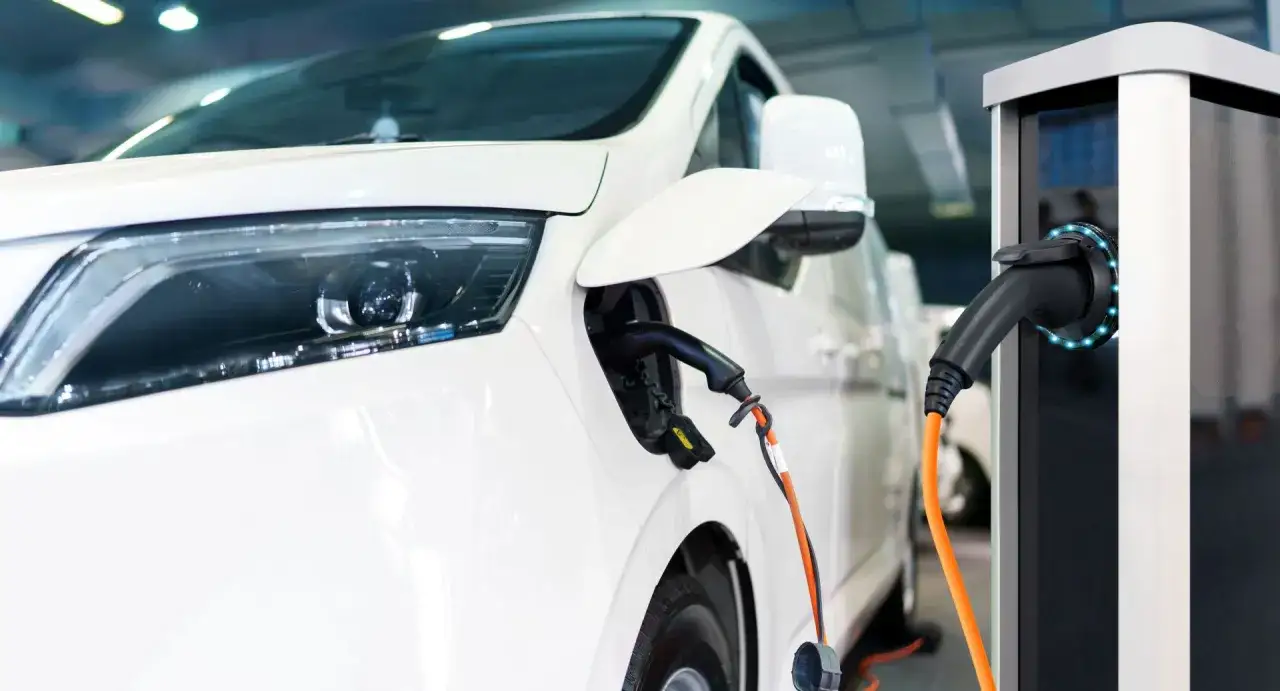 Biały samochód elektryczny podłączony do ładowarki. To przyszłość transportu, którą wspiera program