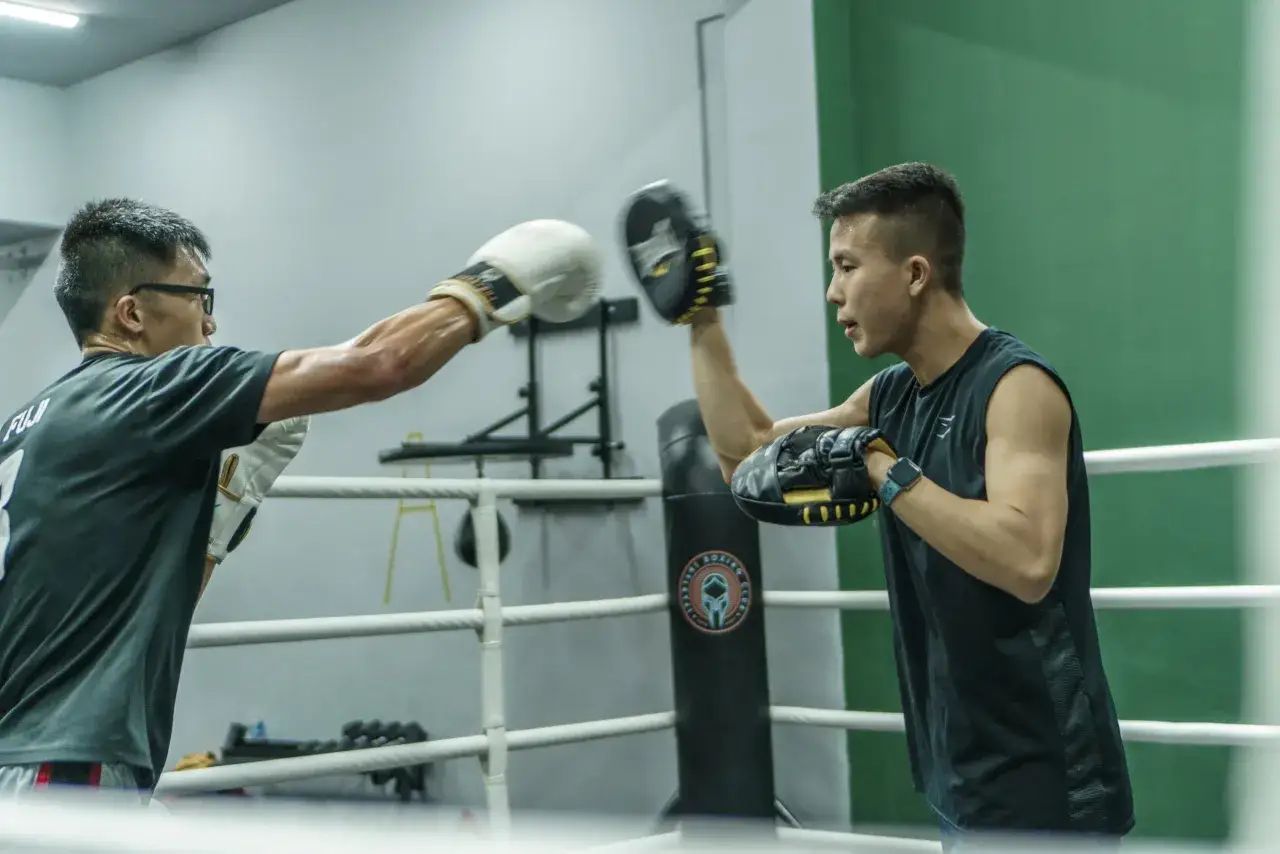 Two boxers spar in a ring. One throws a punch while the other dodges. This intense training shows how many hours boxers train a day.