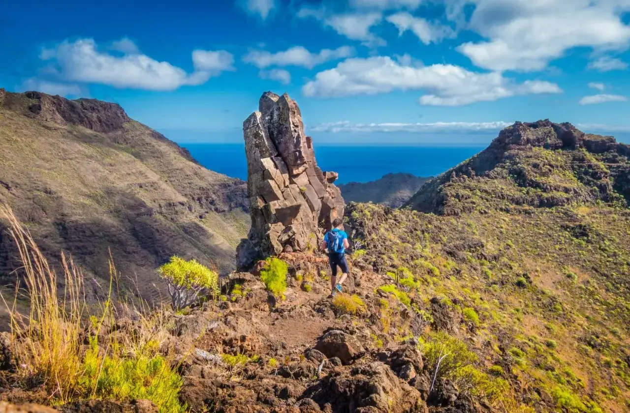 Un randonneur explore un sentier escarpé à Tenerife, dominant l'océan bleu sous un ciel éclatant.