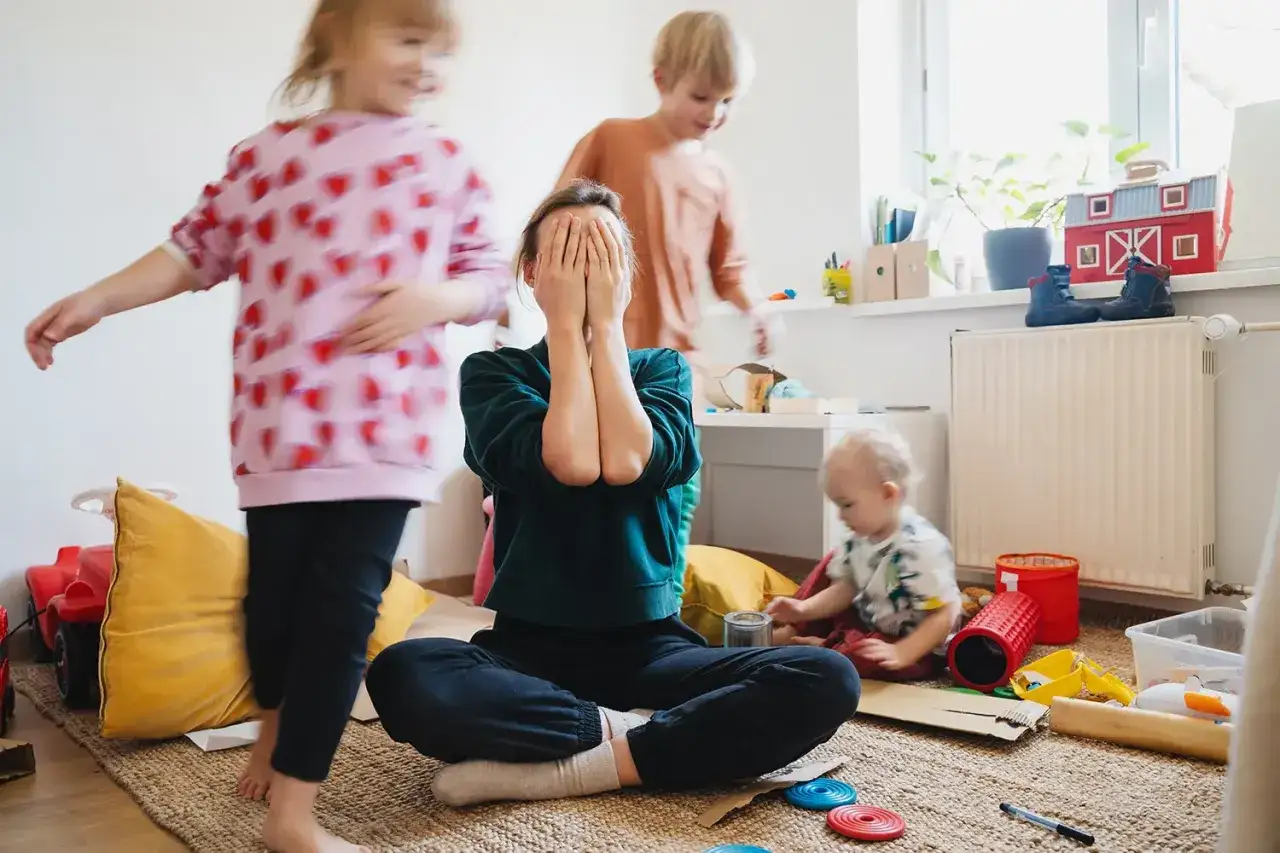 Mutter mit verdecktem Gesicht inmitten spielender Kinder. Ein Beispiel f&uuml;r erziehung ohne schimpfen, wenn die Nerven blank liegen.