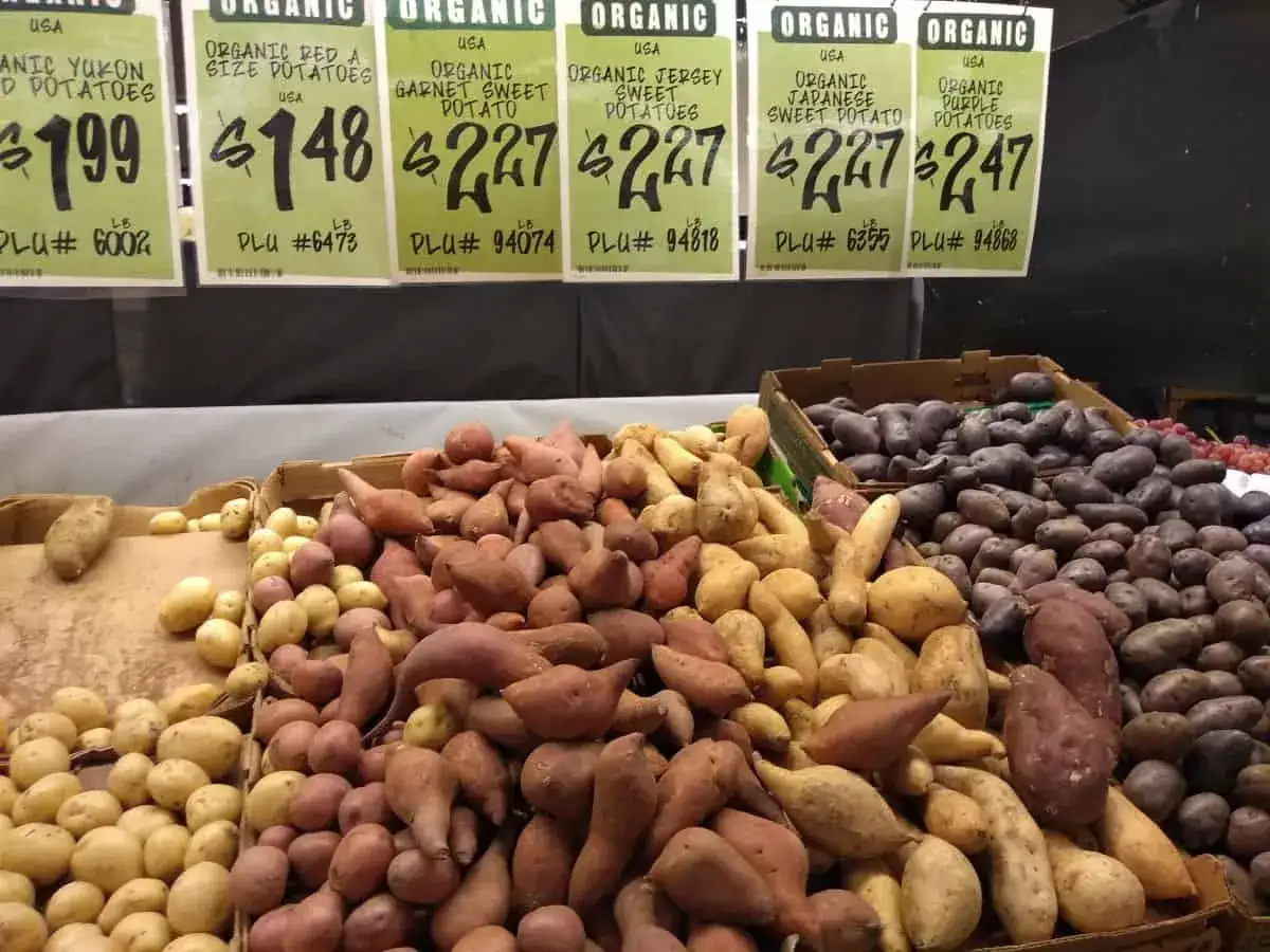 Bunte Auswahl an Bio-Kartoffeln und tropischen Süßkartoffeln, darunter Garnet Sweet Potatoes, in Kisten und auf einem Tresen.