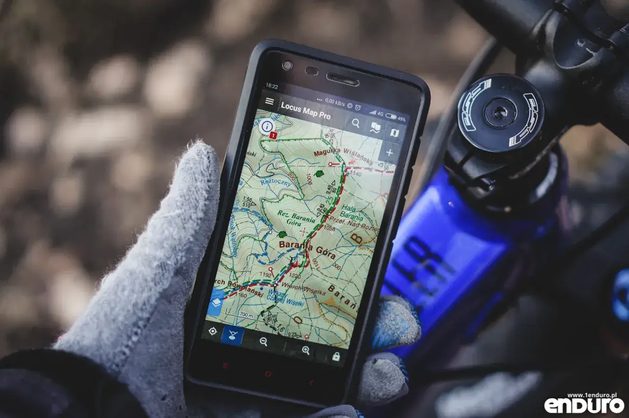 Rękawiczka trzyma telefon z mapą terenową, pokazującą szlak. To idealny gps w rowerze na górskie wyprawy.