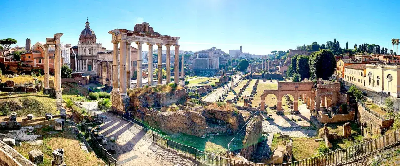 Antiche rovine romane sotto un cielo azzurro, dove si trova il Foro Romano, con colonne imponenti e resti di edifici.