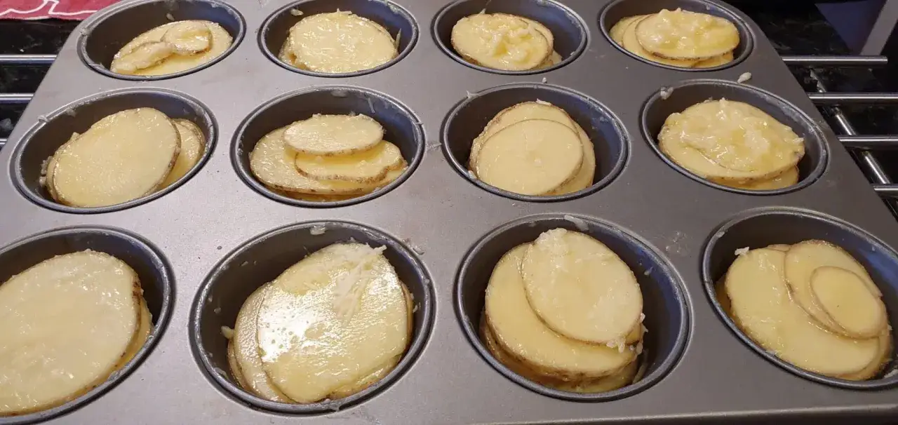 Tunna skivor av potatis i muffinsformar, redo att bakas. En h&auml;rlig syn av potatis i muffinsform!