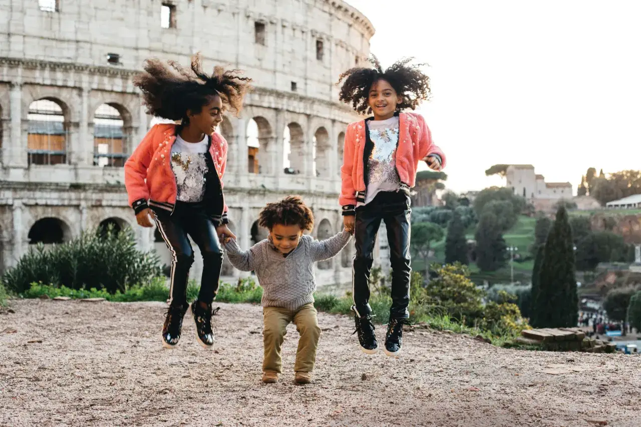 Niños saltando de alegría frente al Coliseo en Roma.