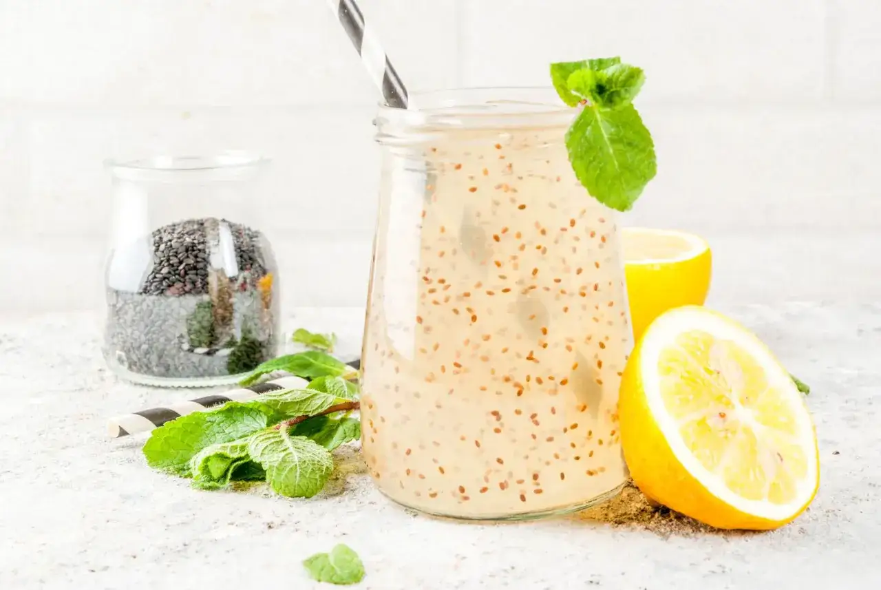 Refrescante agua de chia con limón y menta, lista para disfrutar. Un tarro de semillas de chia al fondo.