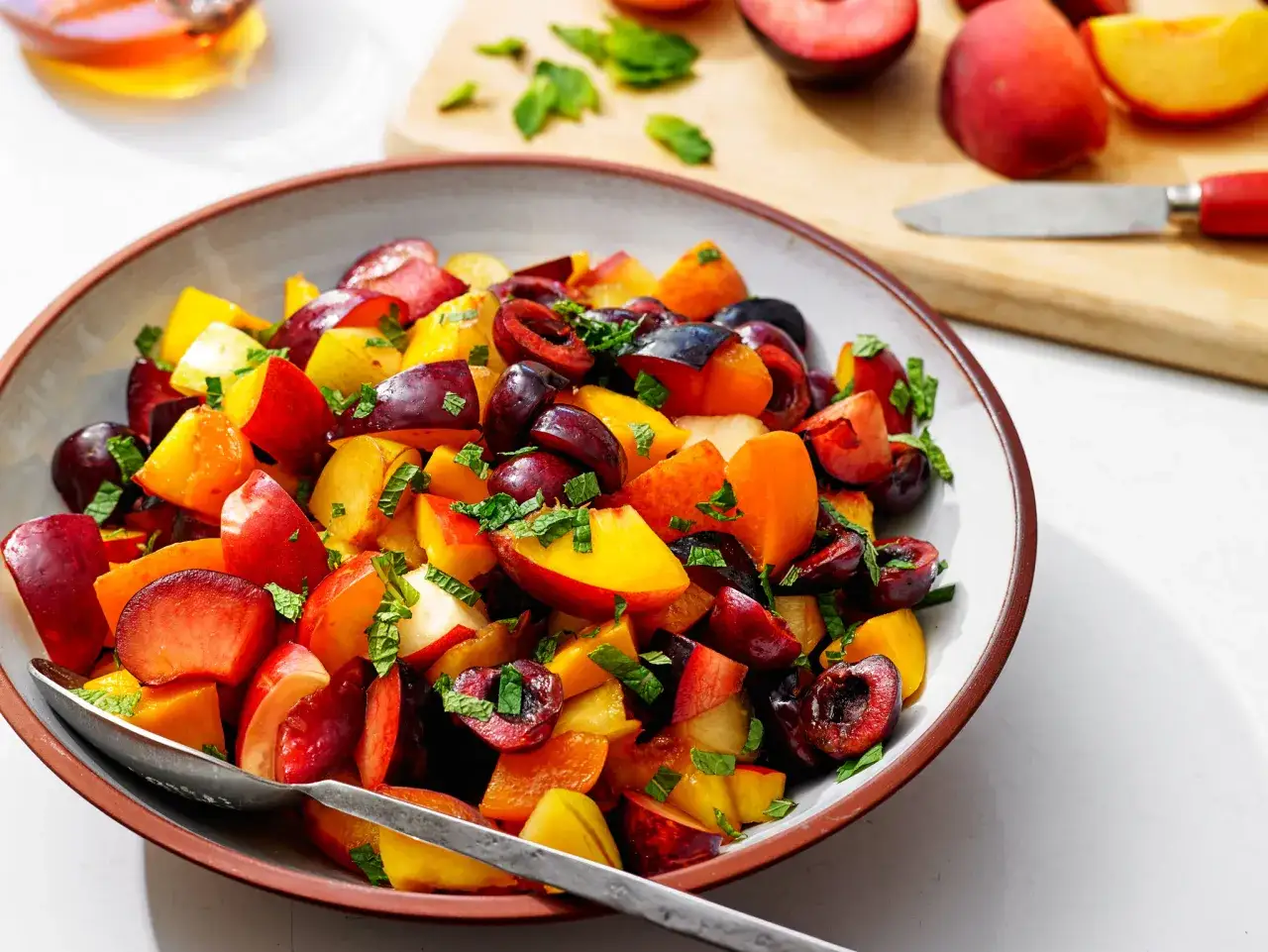 Ein bunter, sommerlicher Obstsalat aus Pflaumen, Pfirsichen und Kirschen, garniert mit Minze.