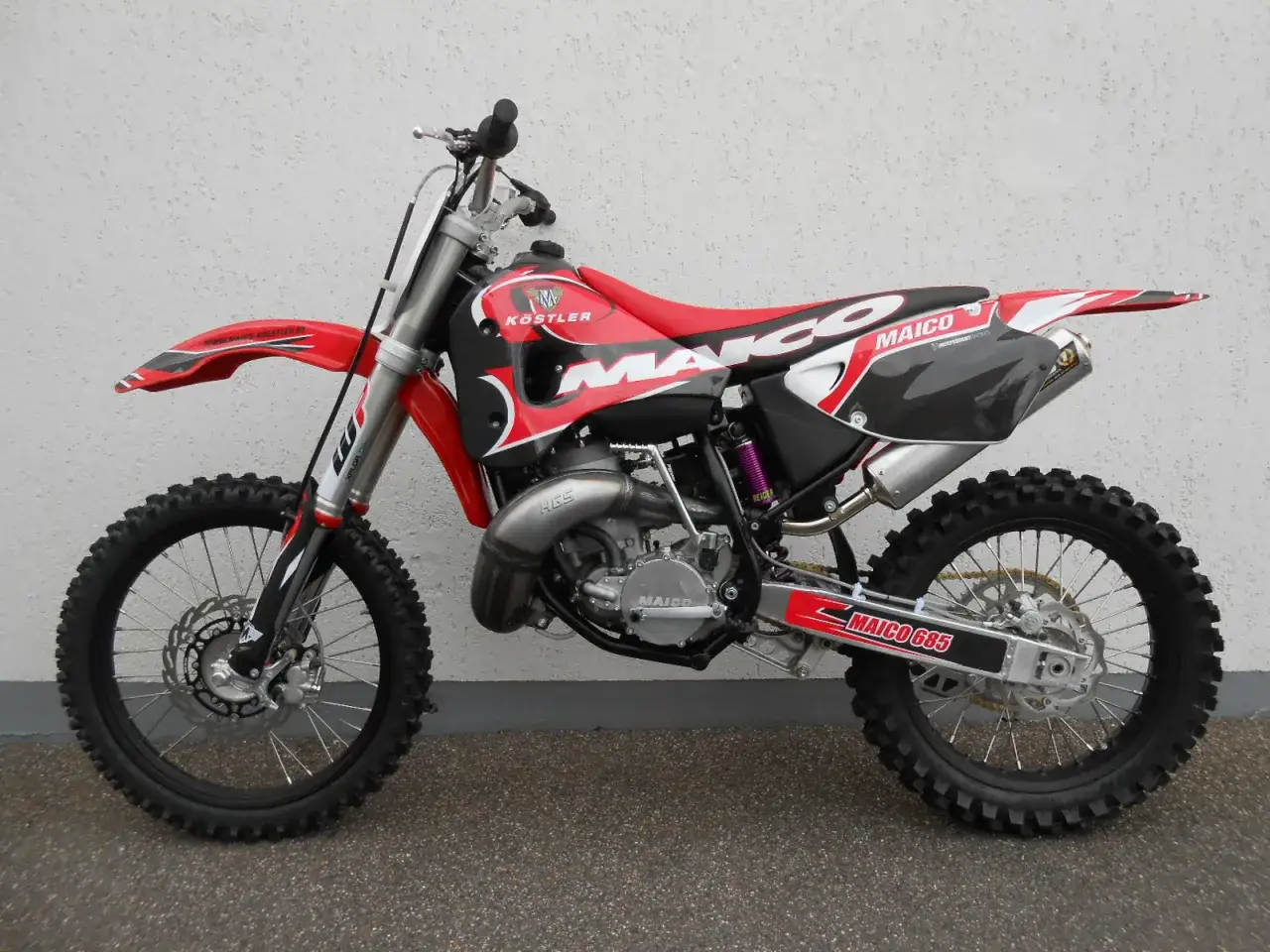 Czerwony motocykl crossowy Maico 700 2T o dużej mocy, z czarnymi i białymi detalami, gotowy do jazdy po torze.