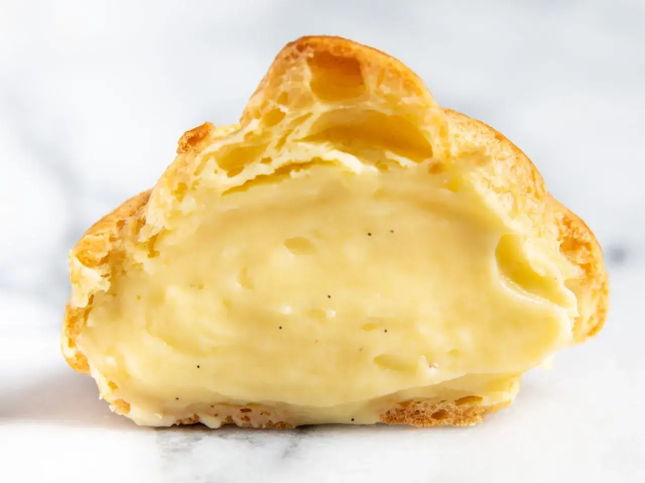 Profiterol relleno de cremosa crema pastelera sin azucar, con motas de vainilla visibles.