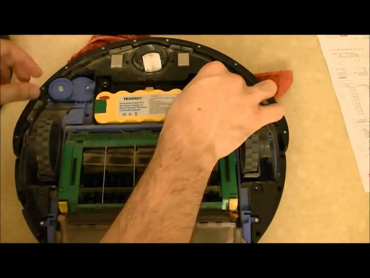 Mano arreglando un Roomba con **error 15**. Se ve la bater&iacute;a amarilla y las escobillas.