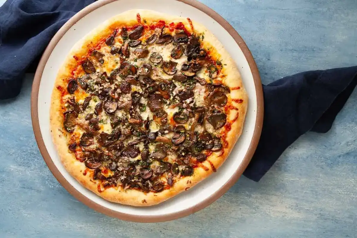 Pizza z grzybami i serem, polana sosem śmietanowym do pizzy.