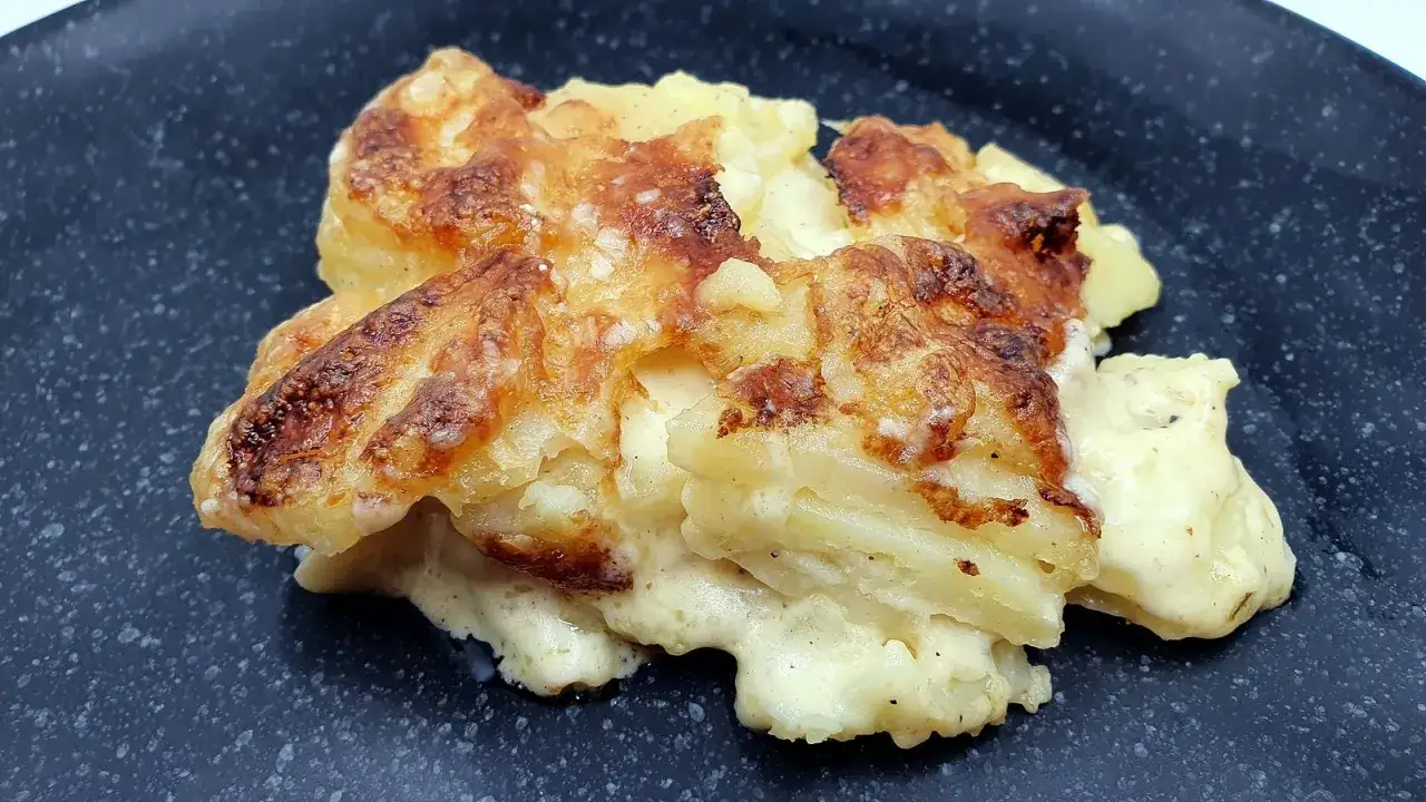 Un déliceux gratin dauphinois cuisson lente, aux pommes de terre fondantes et croûte dorée, servi sur une assiette noire.