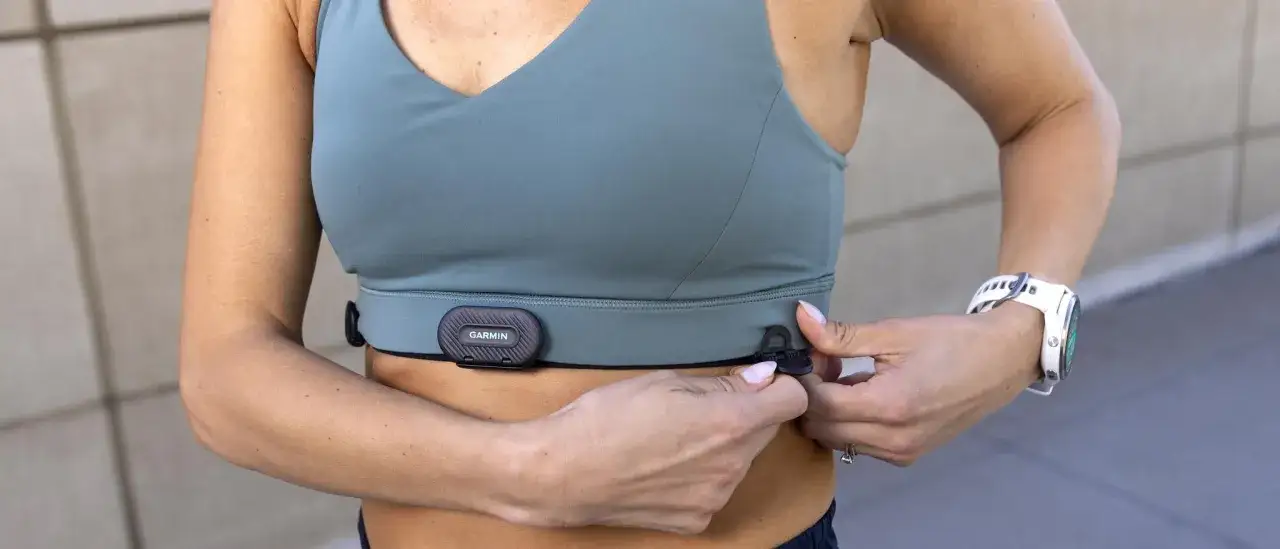 Frau befestigt Garmin Brustgurt f&uuml;r pr&auml;zise Herzfrequenz beim Sport. Eine wei&szlig;e Sportuhr ist am Handgelenk sichtbar.