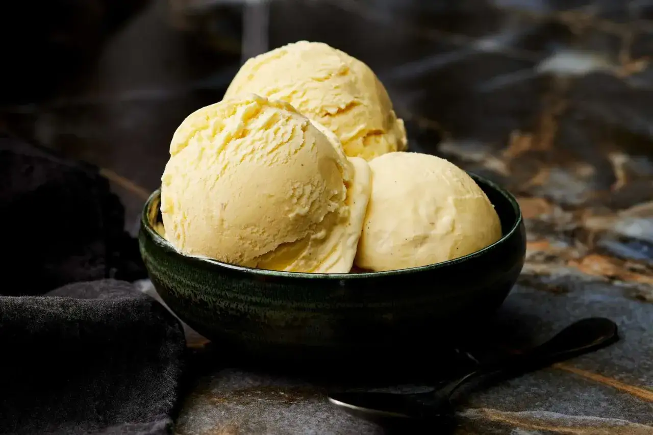Drei Kugeln cremiges Vanilleeis in einer grünen Schale. So wird selbstgemachtes Eis cremig und köstlich.