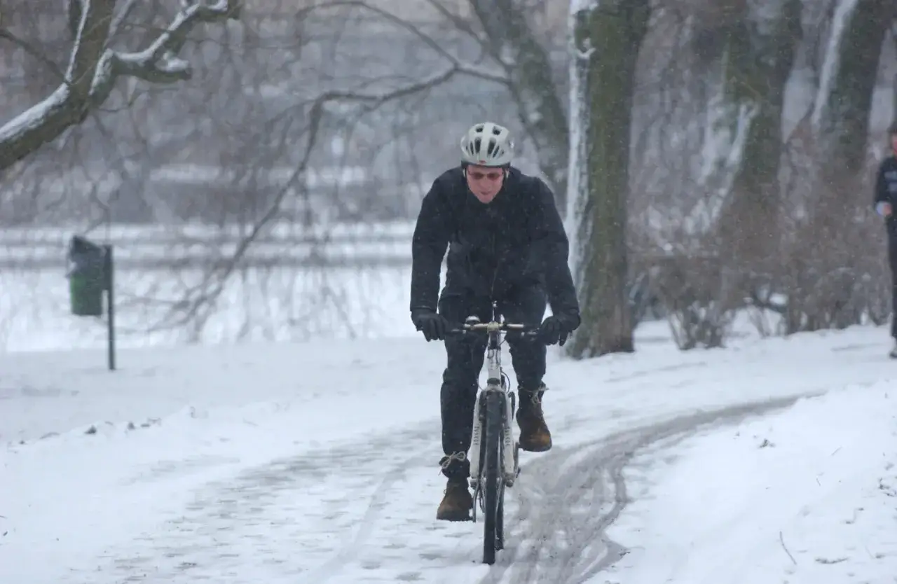 Man cyklar p&aring; vintern i sn&ouml;fall. Han b&auml;r hj&auml;lm och varma kl&auml;der.