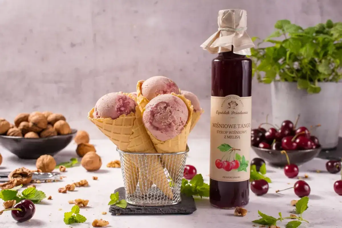 Wafelki z lodami wiśniowymi obok butelki syropu do herbaty