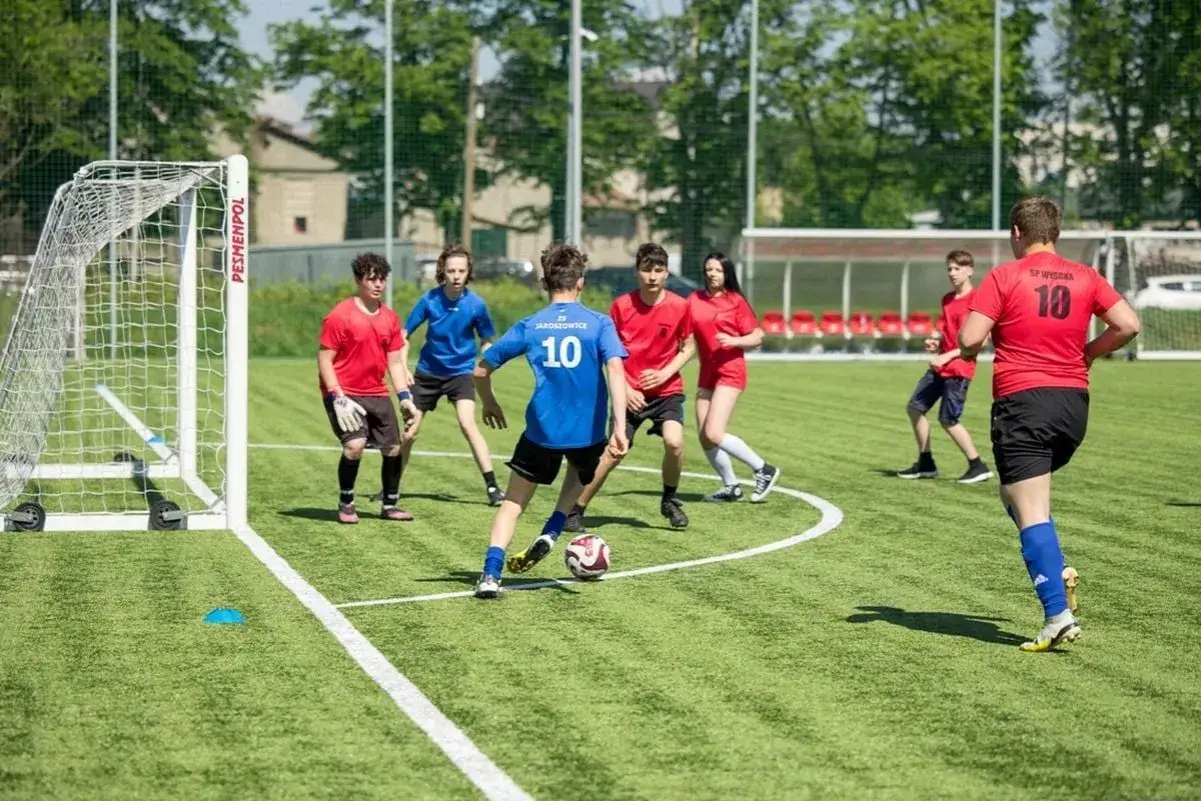 Dzieci i młodzież w akcji na boisku piłkarskim. Zacięte wsp&oacute;łzawodnictwo sportowe, gra toczy się o bramkę.