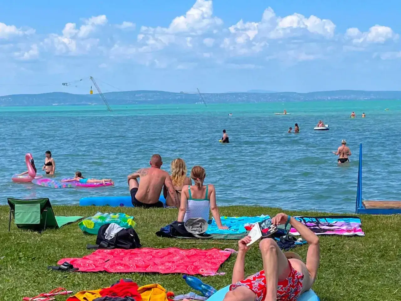 Słoneczny dzień nad Balatonem, ludzie odpoczywają na plaży i kąpią się w wodzie. Idealny czas na camping Balaton.