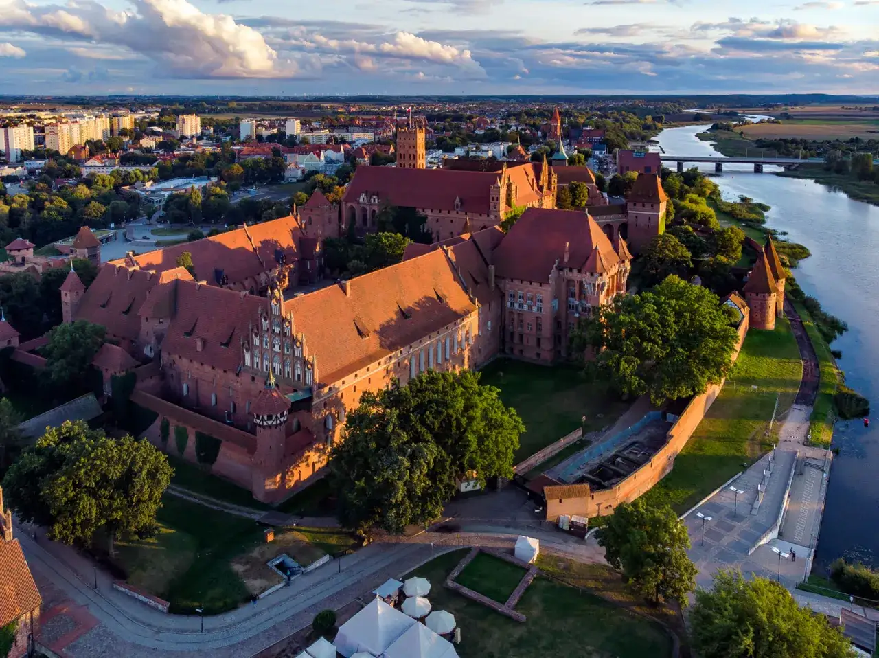 Malbork, największy zamek w Polsce, rozciąga się wzdłuż rzeki Nogat. Czerwona cegła i strzeliste wieże tworzą imponujący widok.