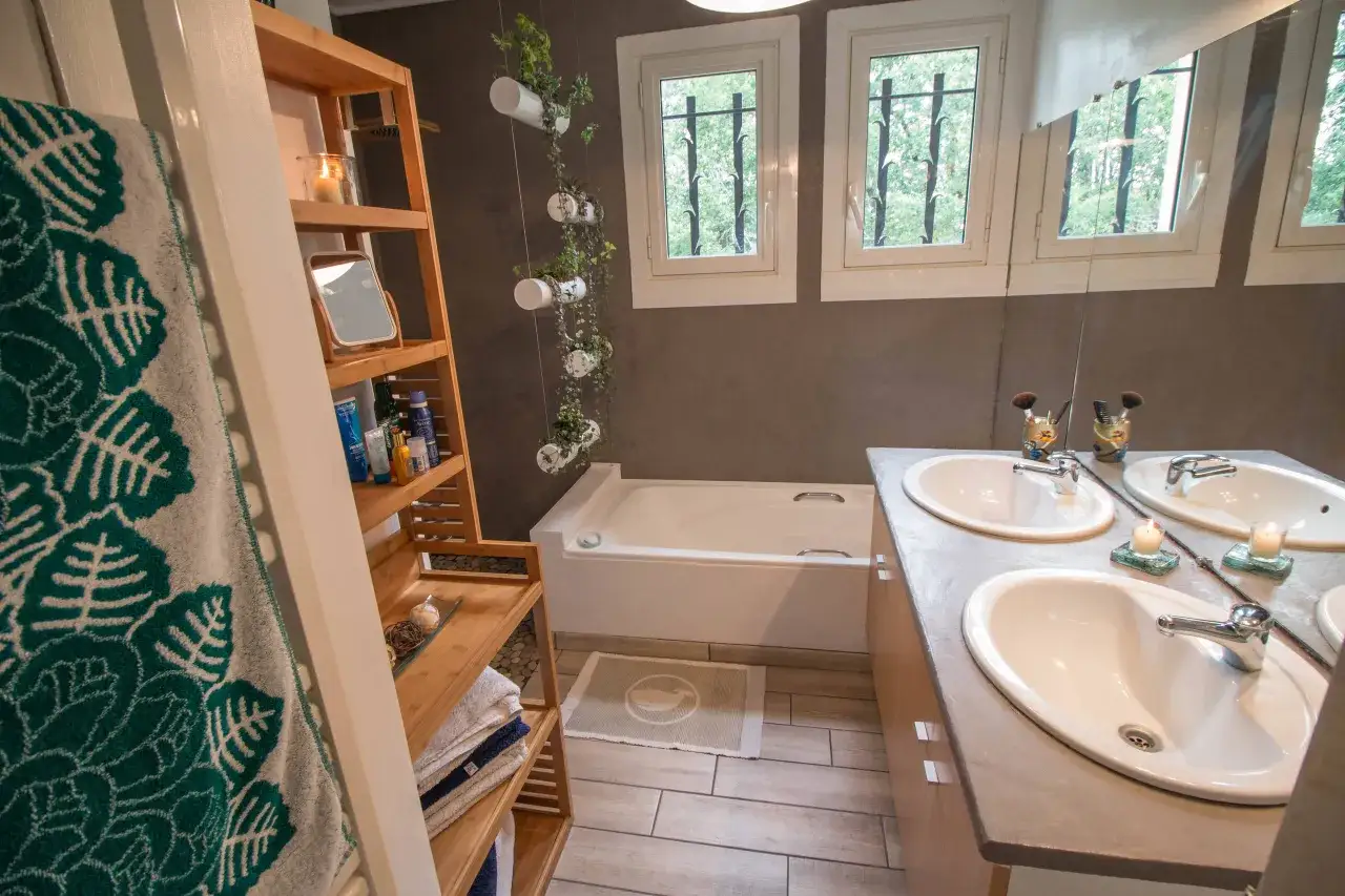 Salle de bain moderne apr&egrave;s r&eacute;novation : baignoire, double vasque, &eacute;tag&egrave;res en bois, plantes suspendues. Une transformation r&eacute;ussie !