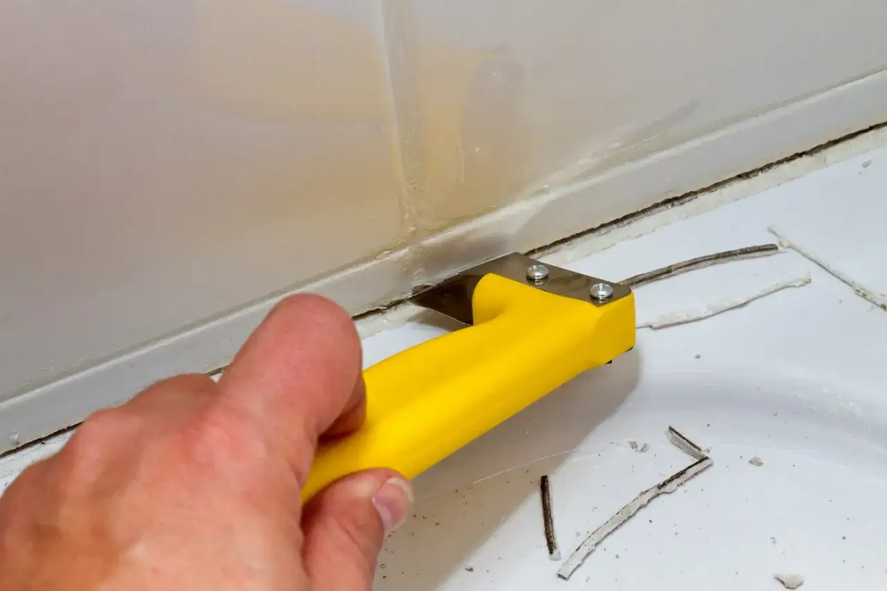 Main tenant utilise un grattoir jaune pour enlever du silicone ancien. Le vinaigre peut aider &agrave; ramollir le silicone avant de l'enlever.