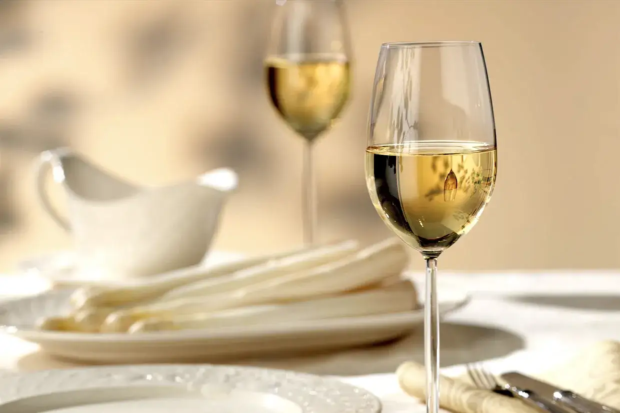 Ein Glas Wei&szlig;wein steht bereit f&uuml;r den Spargel. Im Hintergrund ein weiteres Glas und eine Sauciere.