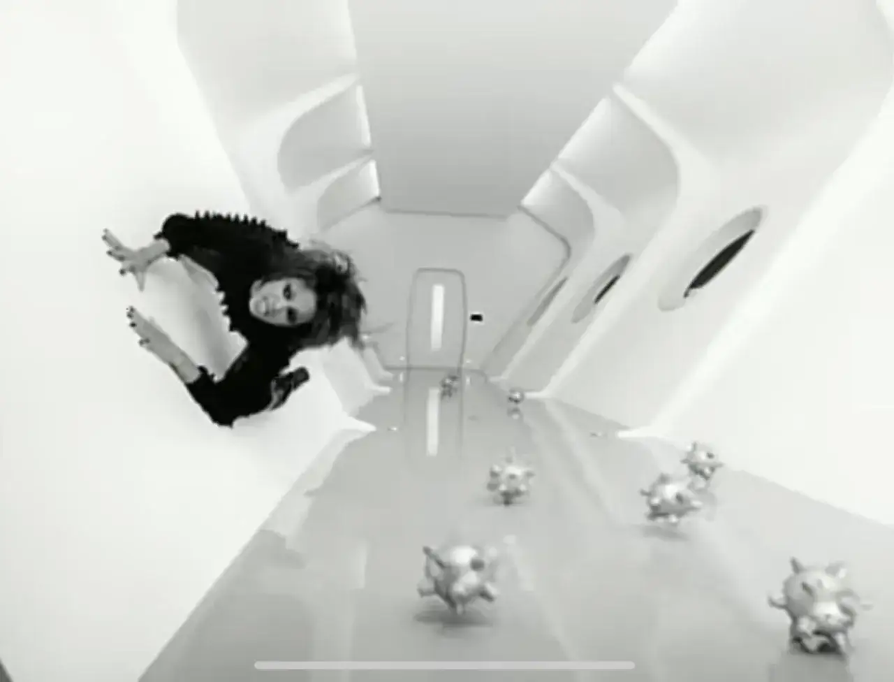 Eine Frau in Schwarz schwebt in einem futuristischen Gang, umgeben von kugelförmigen Objekten. Ein Szene aus dem teuerstes musikvideo aller zeiten.
