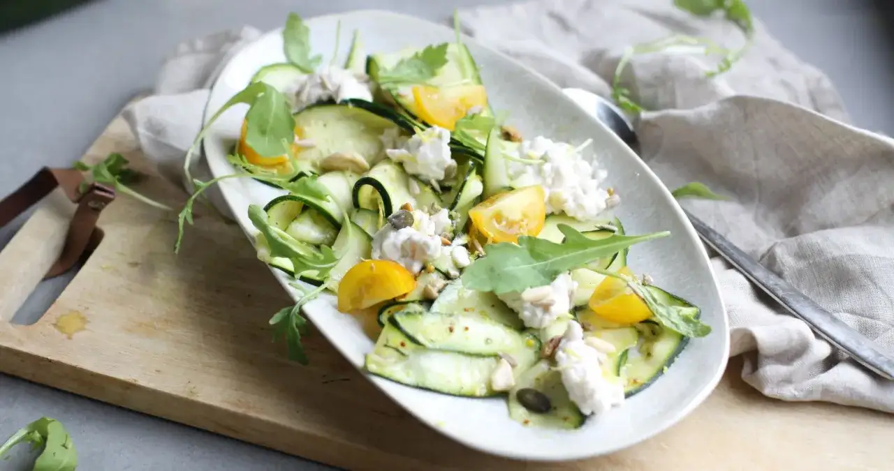 Erfrischender Zucchini Salat mit Ricotta, gelben Tomaten und Rucola, garniert mit Kernen. Ein leichter Genuss.