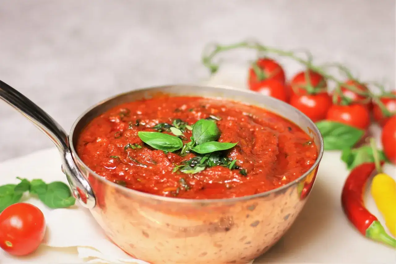 En kopp med hemlagad tomatsås, garnerad med färsk basilika. Perfekt för ditt nästa tomatsås recept.