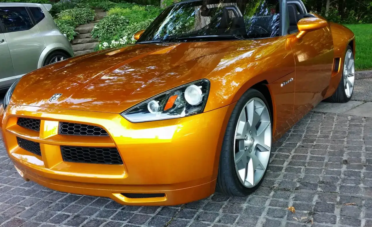 Pomarańczowy roadster z błyszczącym lakierem i masywnymi felgami stoi na brukowanej nawierzchni.