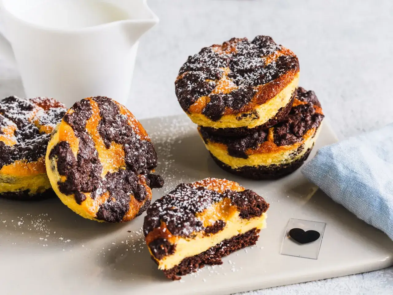 Zupfkuchen Muffins mit Puderzucker bestäubt, ein halber Muffin zeigt die cremige Füllung. Daneben ein Milchkännchen.