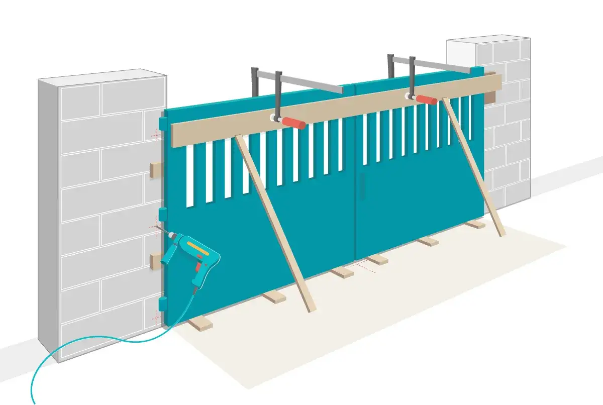 Installation d'un portail battant : une perceuse est utilisée pour fixer les charnières sur un pilier en parpaings. Le portail est soutenu par des tasseaux et des serre-joints.