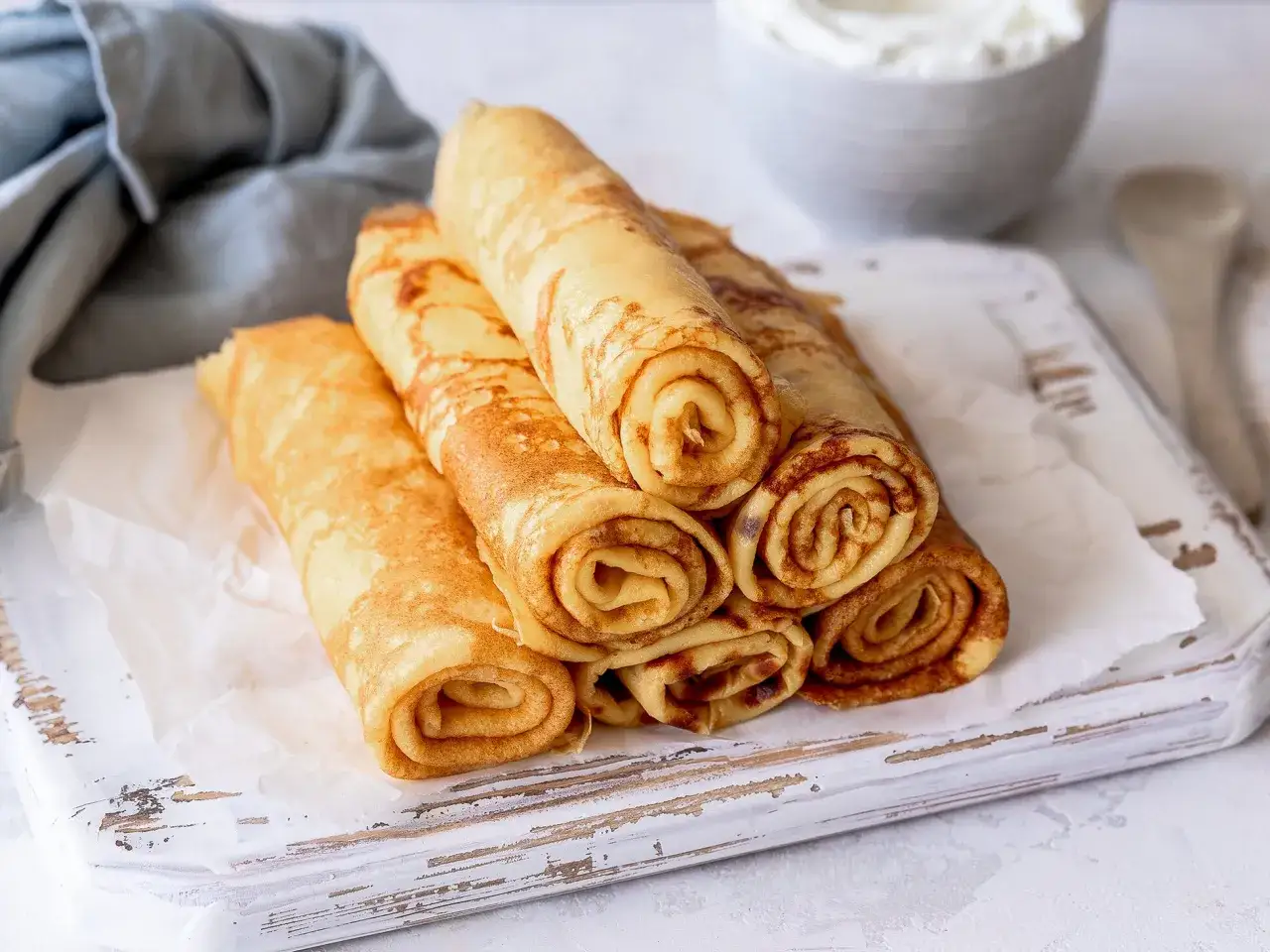 Gestapelte, goldbraune low carb pfannkuchen auf einem wei&szlig;en Brett. Dazu eine Sch&uuml;ssel mit Sahne und ein Holzl&ouml;ffel.