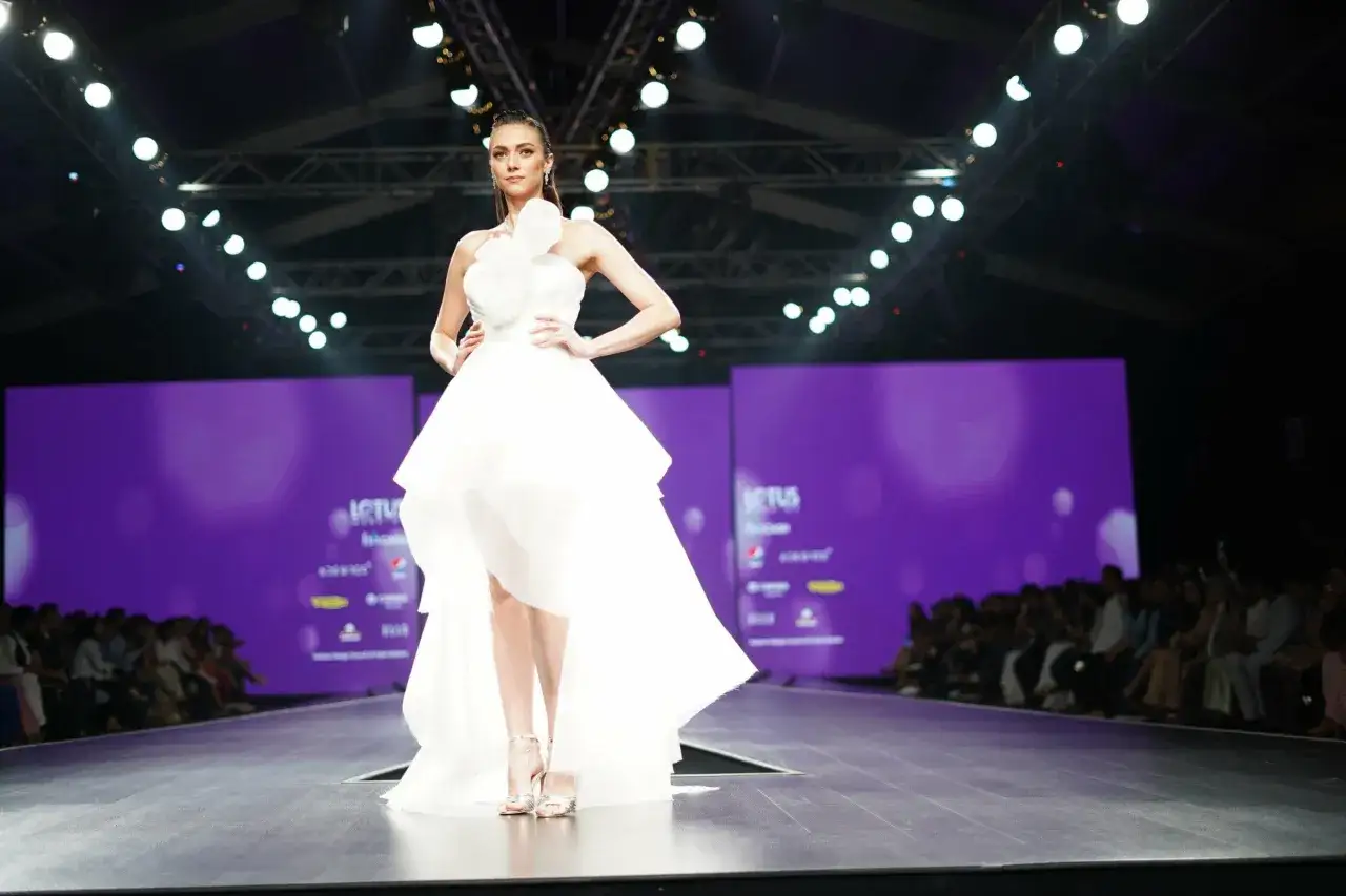 A model showcases a stunning white gown with a dramatic bow detail on a runway, embodying high fashion.