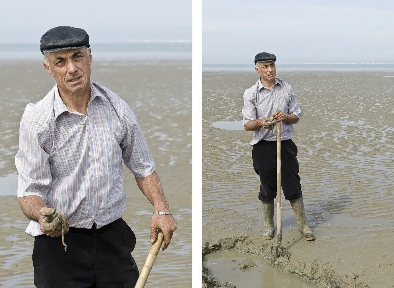 Mężczyzna w czapce i pasiastym swetrze zbiera coś z błota na plaży. Jego dłonie, jakby uchwycone przez przysłonę w aparacie fotograficznym, trzymają narzędzie i zdobycz.