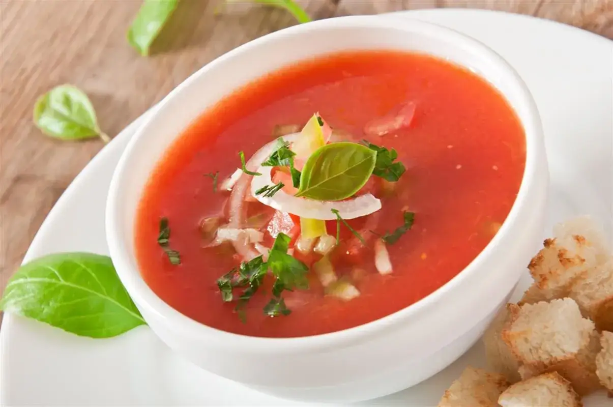 Chłodnik gazpacho, kwintesencja hiszpańskiego jedzenia, podany z grzankami i świeżą bazylią.